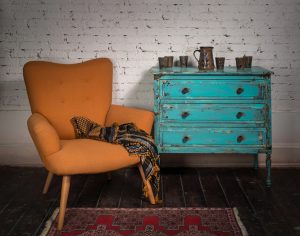 Composition of vintage orange armchair, blue cabinet and ornate scarf in studio