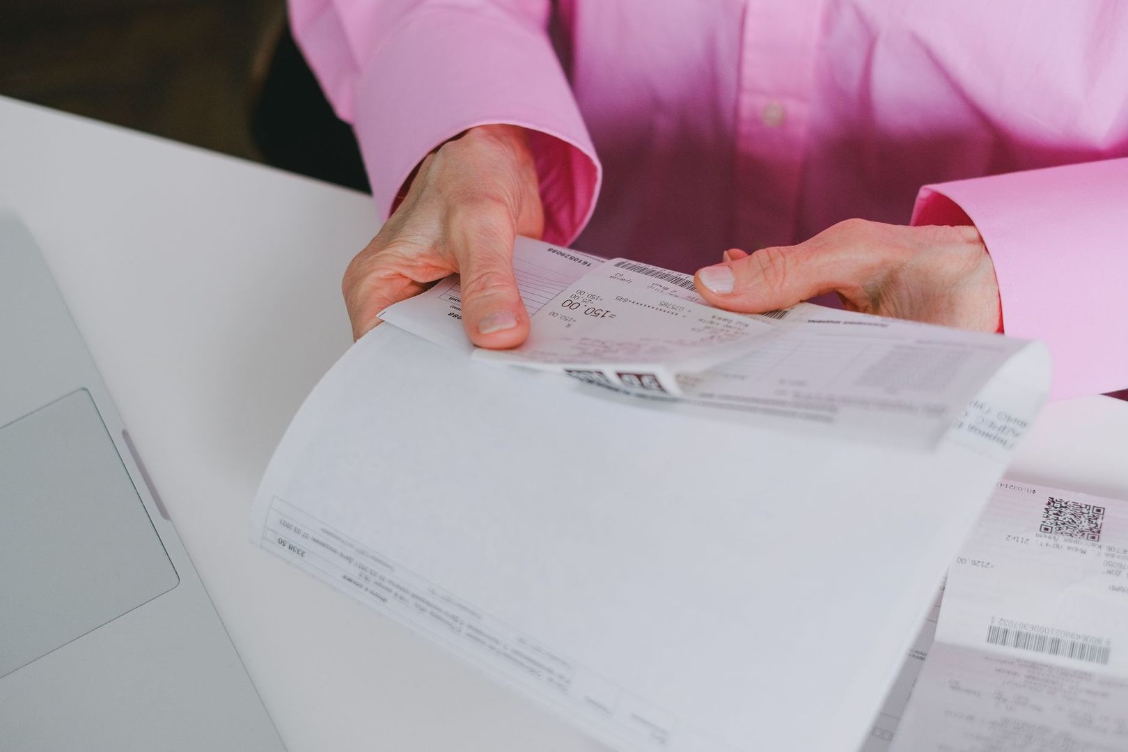 En person i rosa skjorte går gjennom ubetalte fakturaer og kvitteringer.