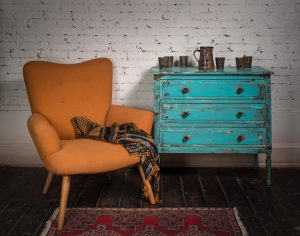 Composition of vintage orange armchair, blue cabinet and ornate scarf in studio
